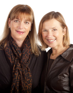 Two women standing next to each other in front of a white background.