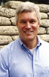 A man in a blue shirt standing next to a wall.
