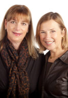 Two women standing next to each other in front of a white background.