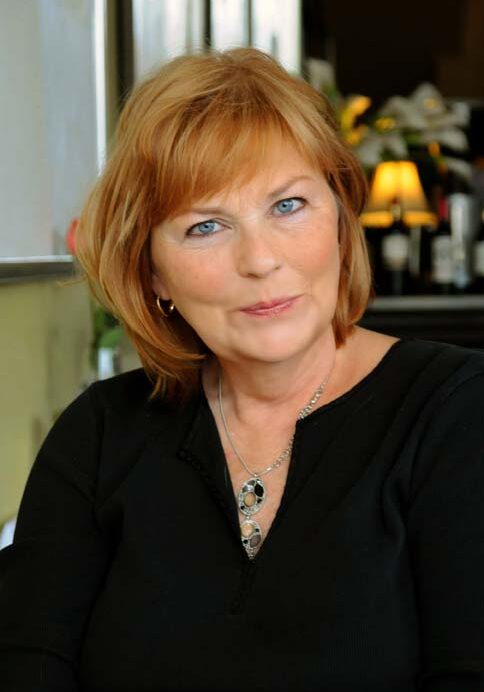 A woman with red hair and wearing black is smiling.