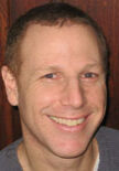 A man smiling for the camera with his head turned to the side.