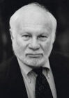 A man with white hair and beard wearing a suit.